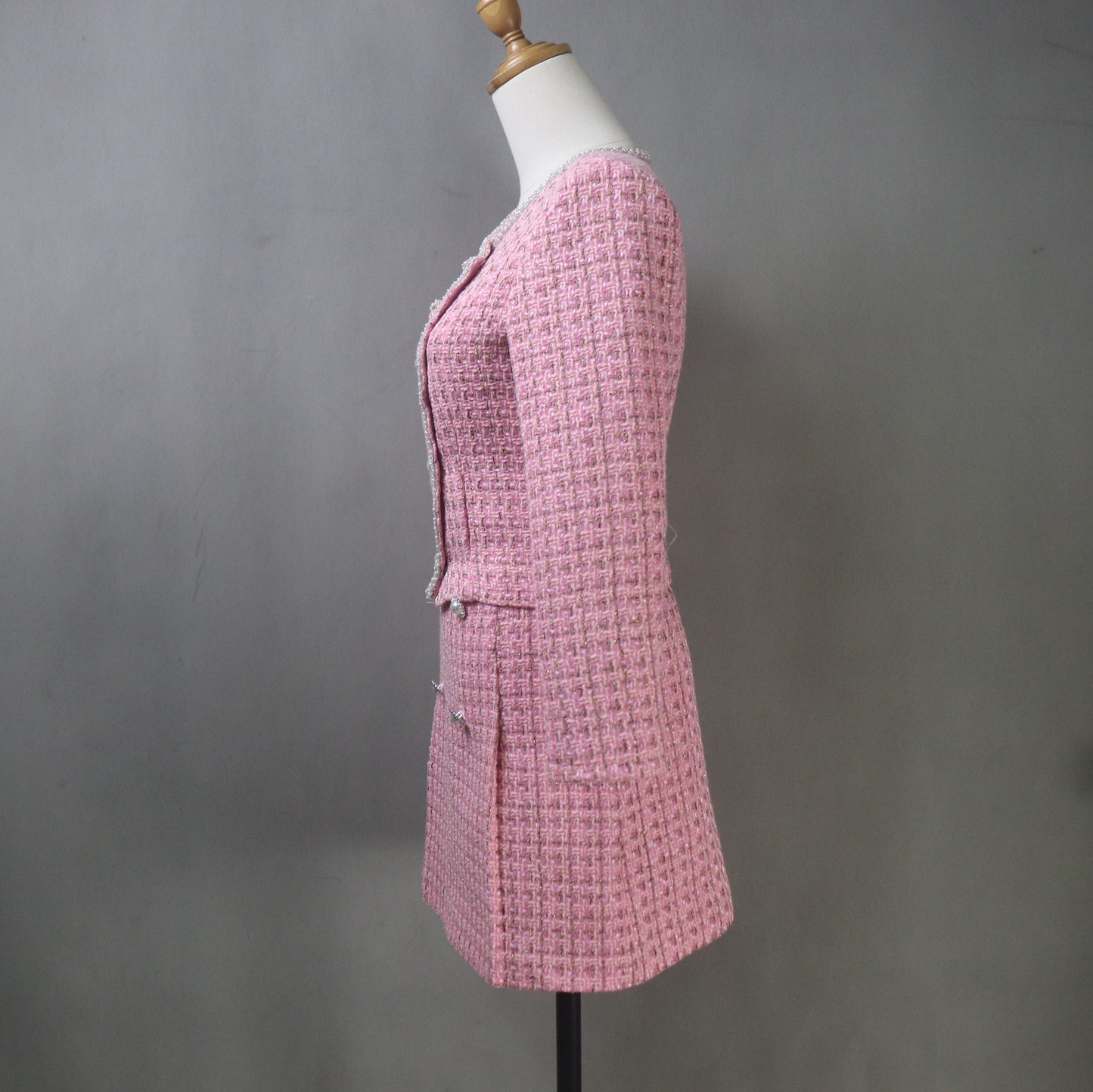 Side view of a pink tweed plus-size skirt suit on a mannequin, showing tailored fit and structured jacket with asymmetrical front button and short skirt.