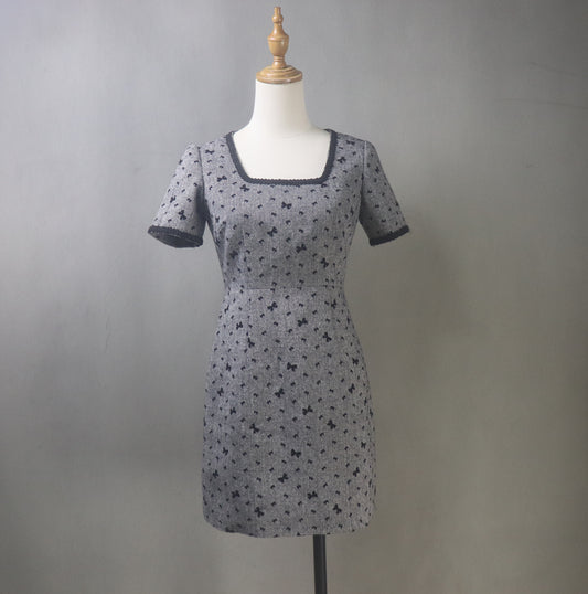 Front view of bespoke dark grey tweed dress on mannequin, featuring square neckline, tailored fit, and delicate bow accents, available in mini or midi length