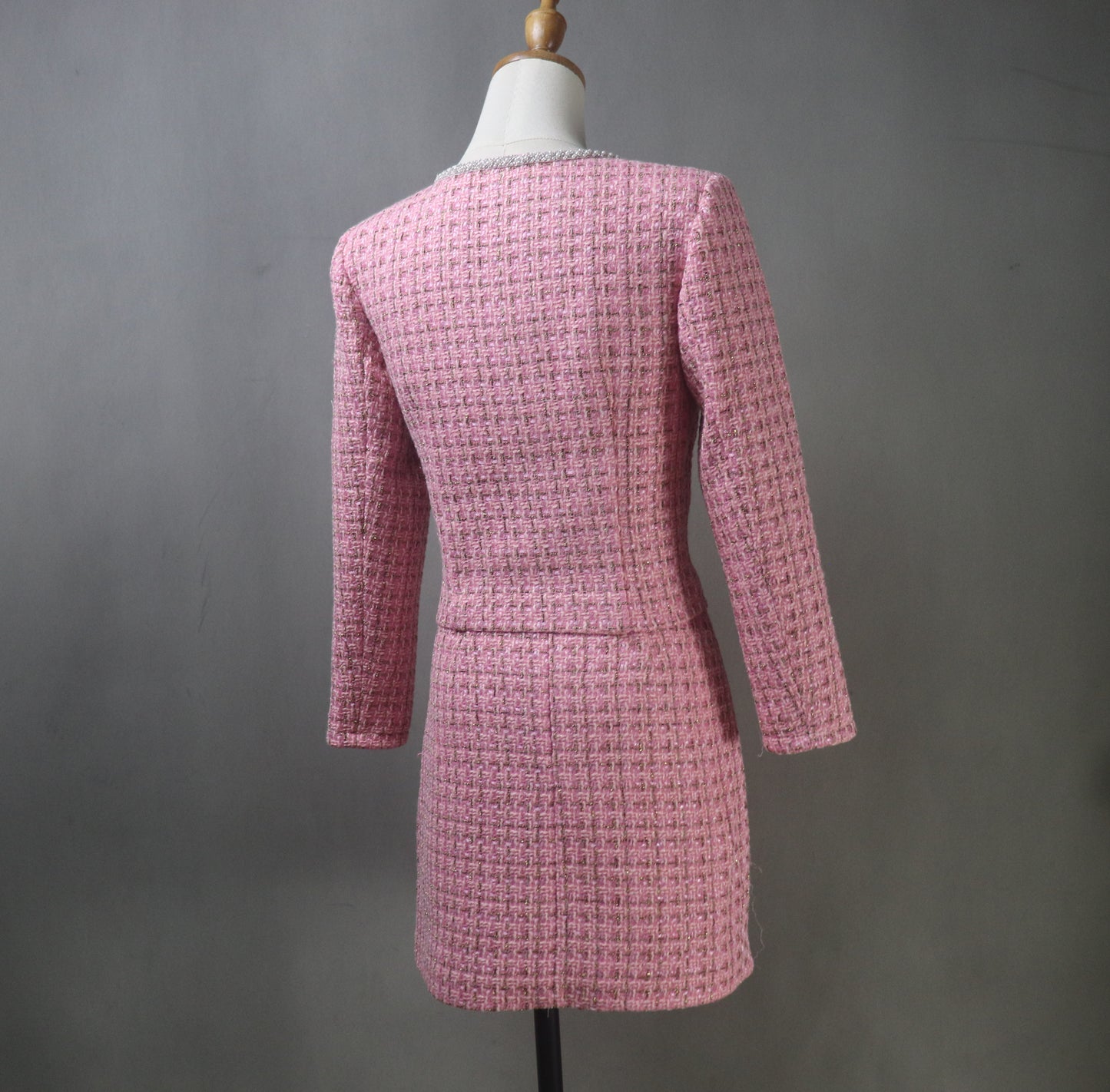 Back view of bespoke pink tweed plus-size skirt suit on a mannequin, highlighting the clean tailored lines of the jacket and short skirt hem.