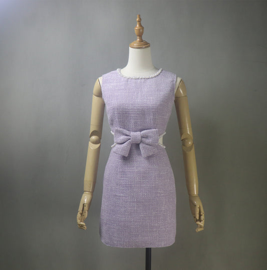 Front view of a bespoke lilac purple tweed dress featuring a pearl-trimmed neckline, decorative bow at the waist, and a stylish cut-out detail. The dress is fitted, sleeveless, and available in mini or midi length, perfect for weddings, graduations, and summer parties.