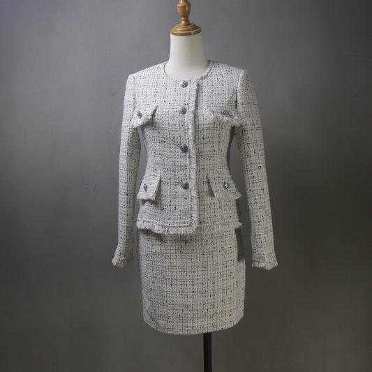 Bespoke beige tweed skirt suit with fringe trim, featuring a fitted long-sleeve jacket with decorative pockets and matching above-knee skirt, displayed on a dress form against a plain gray background