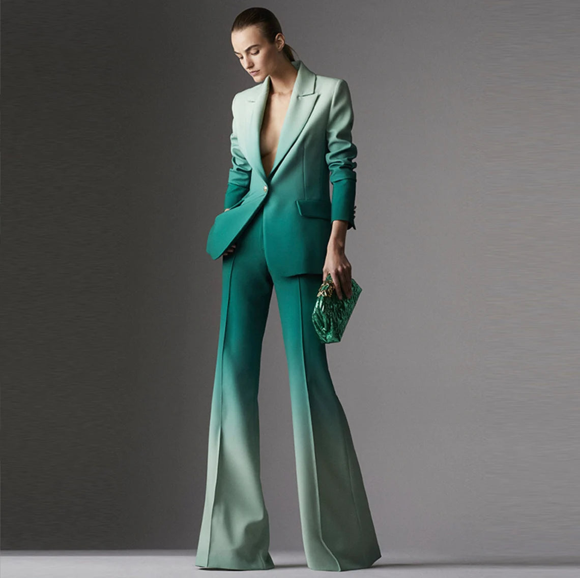 The blazer is the centerpiece of this ensemble, exuding luxury and style. It's meticulously crafted from a rich, emerald green fabric that seamlessly transitions into a subtle gradient, fading into a slightly lighter shade towards the bottom. The luxurious material drapes elegantly, giving the blazer a fluid and sophisticated appearance. The tailored fit ensures it flatters your figure, with structured shoulders and a cinched waist to accentuate your curves.