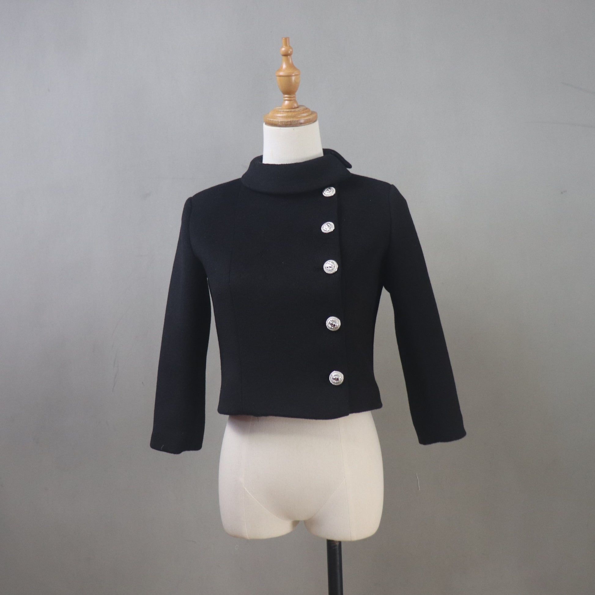Black jacket with silver buttons on a mannequin against a gray background