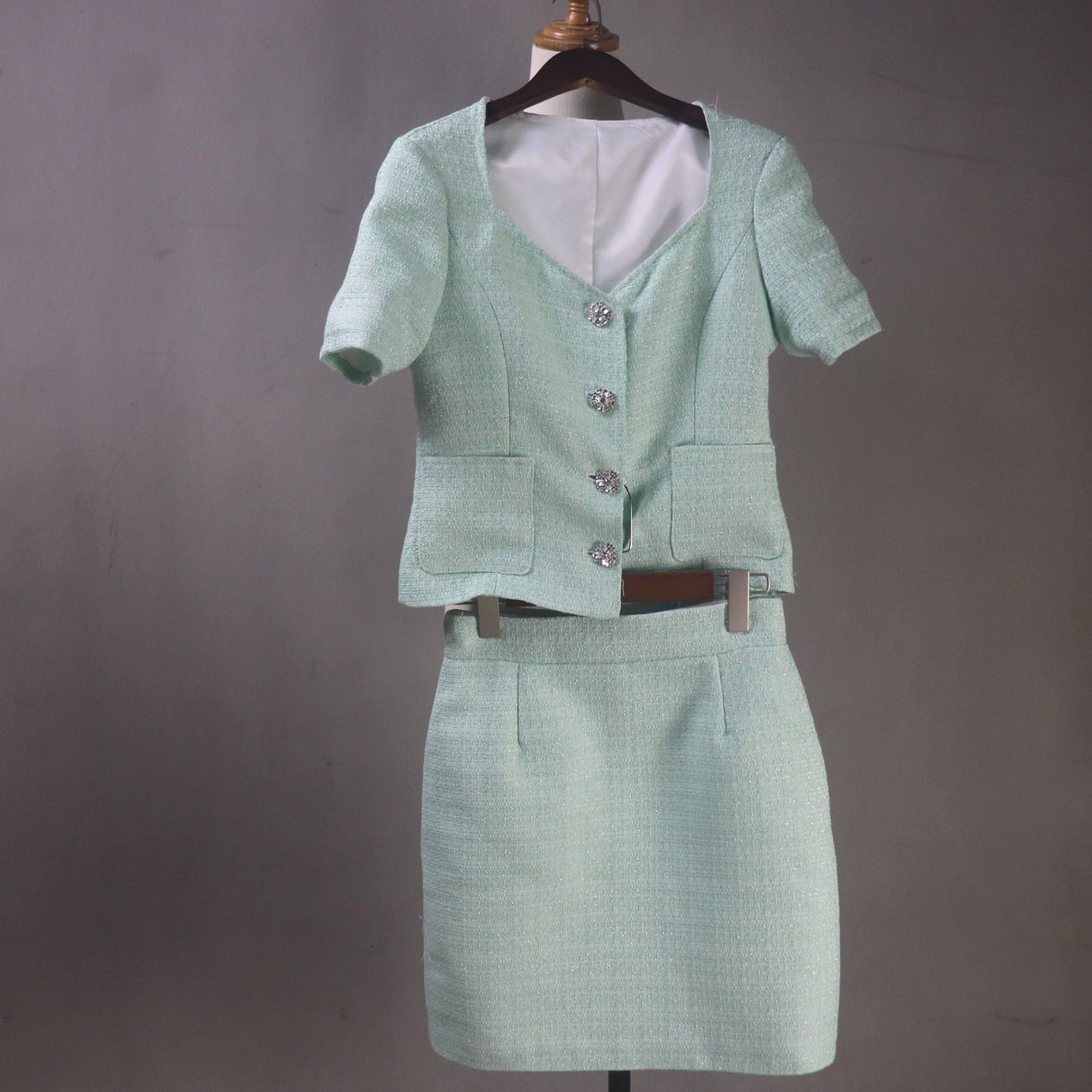 Green two-piece suit with jacket and skirt on a mannequin against a gray background