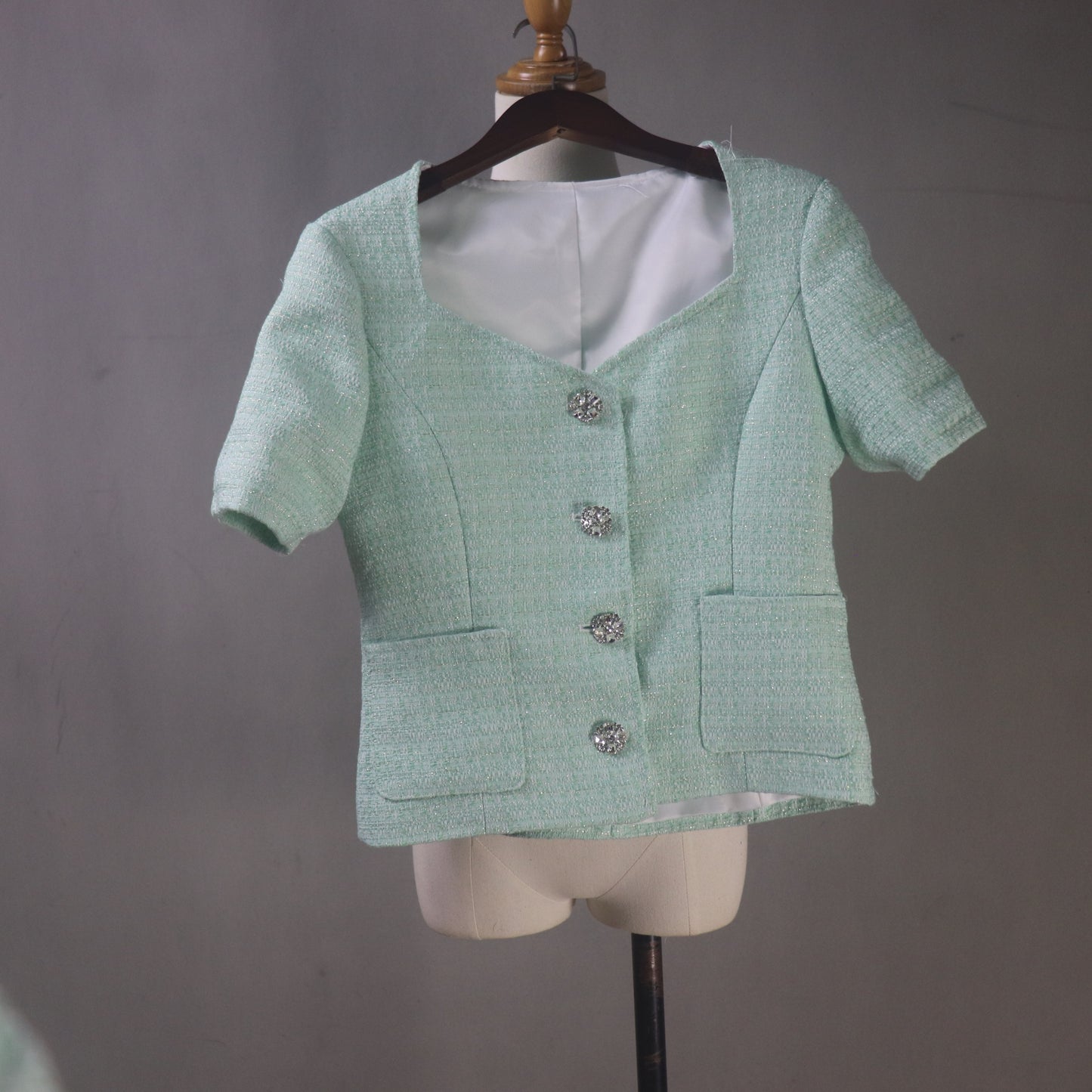 Green textured blazer with buttons on a mannequin against a gray background