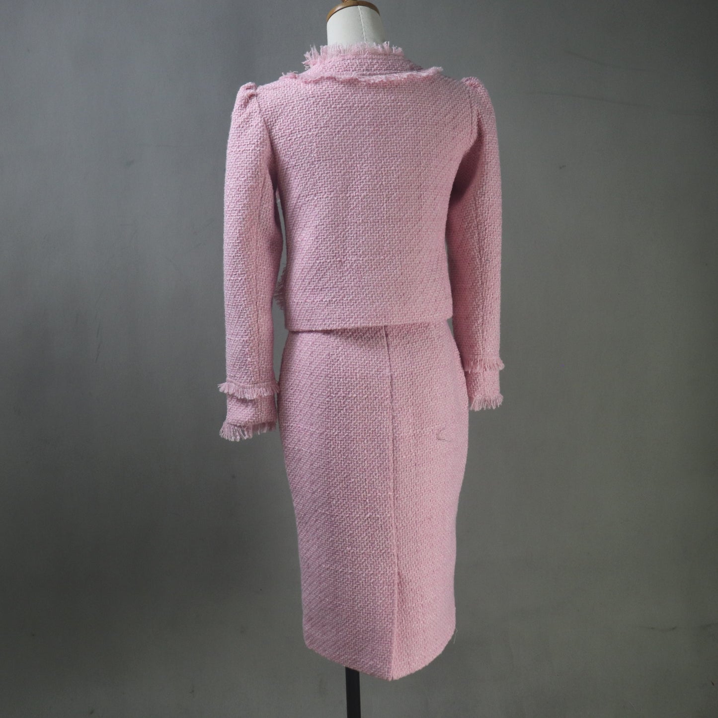 Pink tweed suit on a mannequin against a gray background