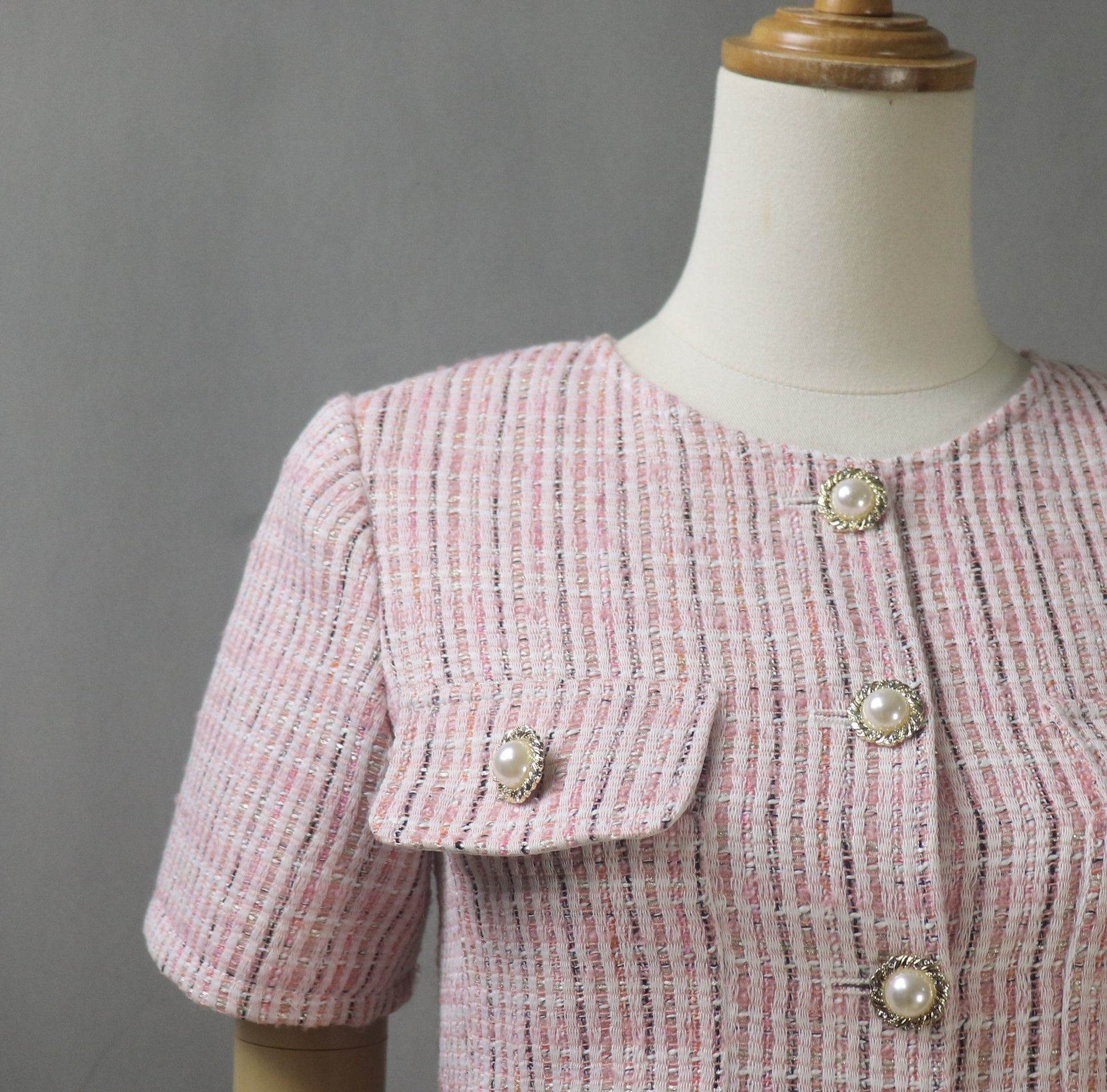 Close-up of pink tweed fabric showing texture, detailed stitching, and decorative gold-tone buttons on the blazer for an elegant finish.