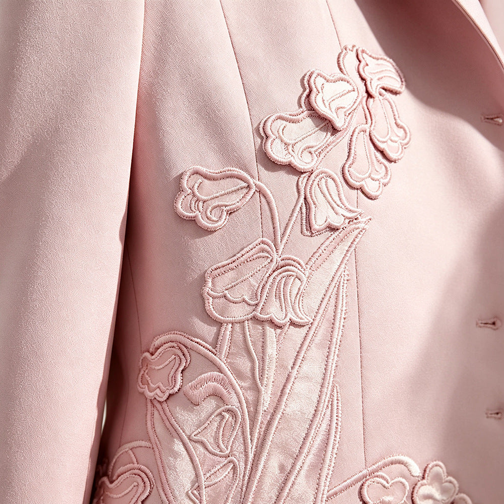Close-up of a light pink tailored jacket or blazer with ornate floral embroidery and applique on the front.