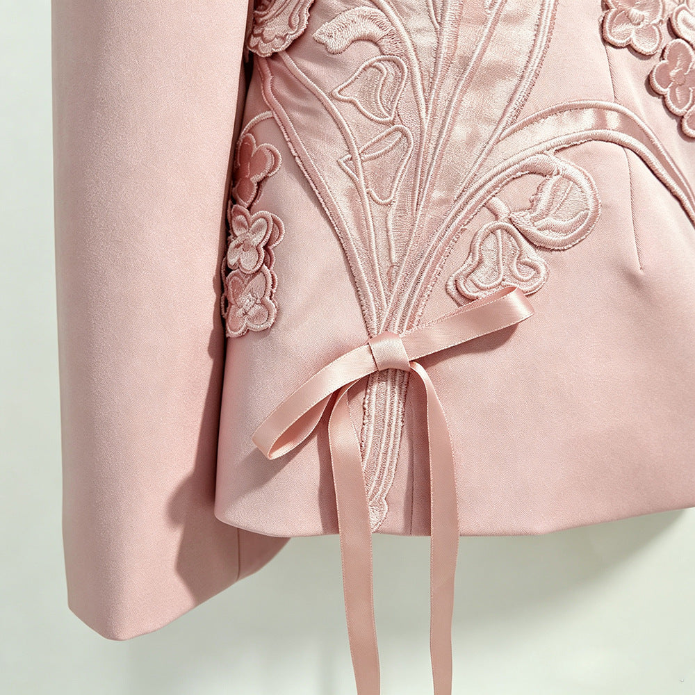 Close-up of a light pink garment featuring floral embroidery, a matching pink ribbon bow, and a soft satin finish against a pale background.