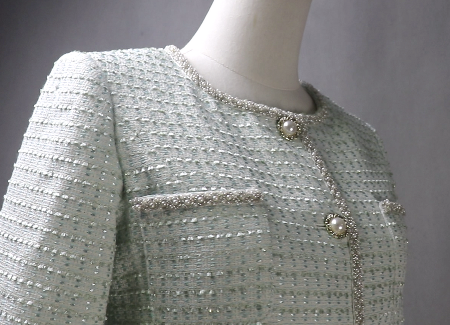 Light gray textured jacket with pearl buttons on a mannequin against a neutral background