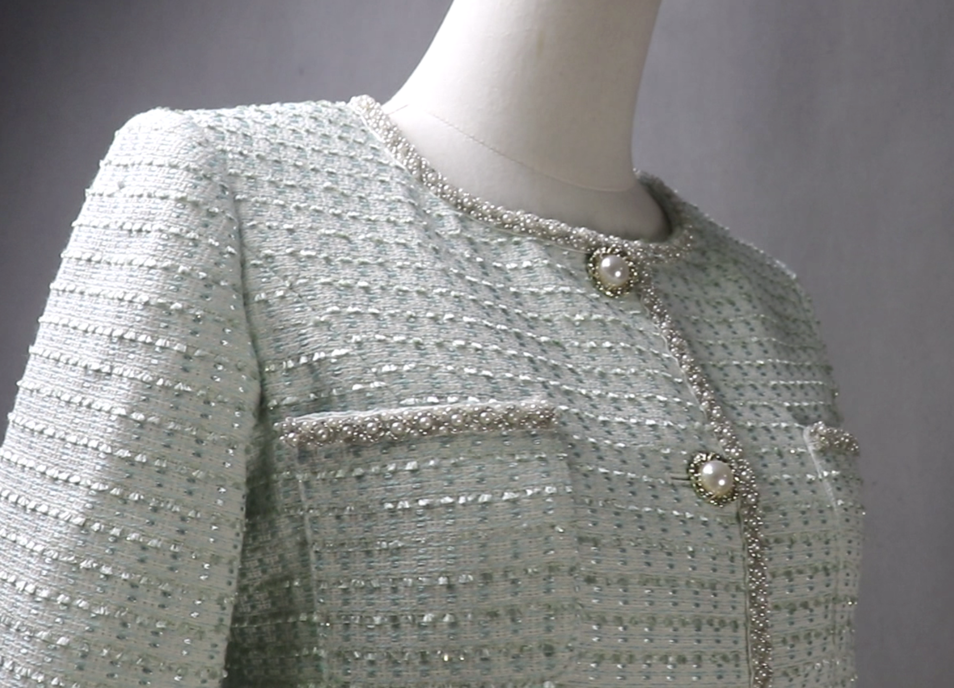 Light gray textured jacket with pearl buttons on a mannequin against a neutral background