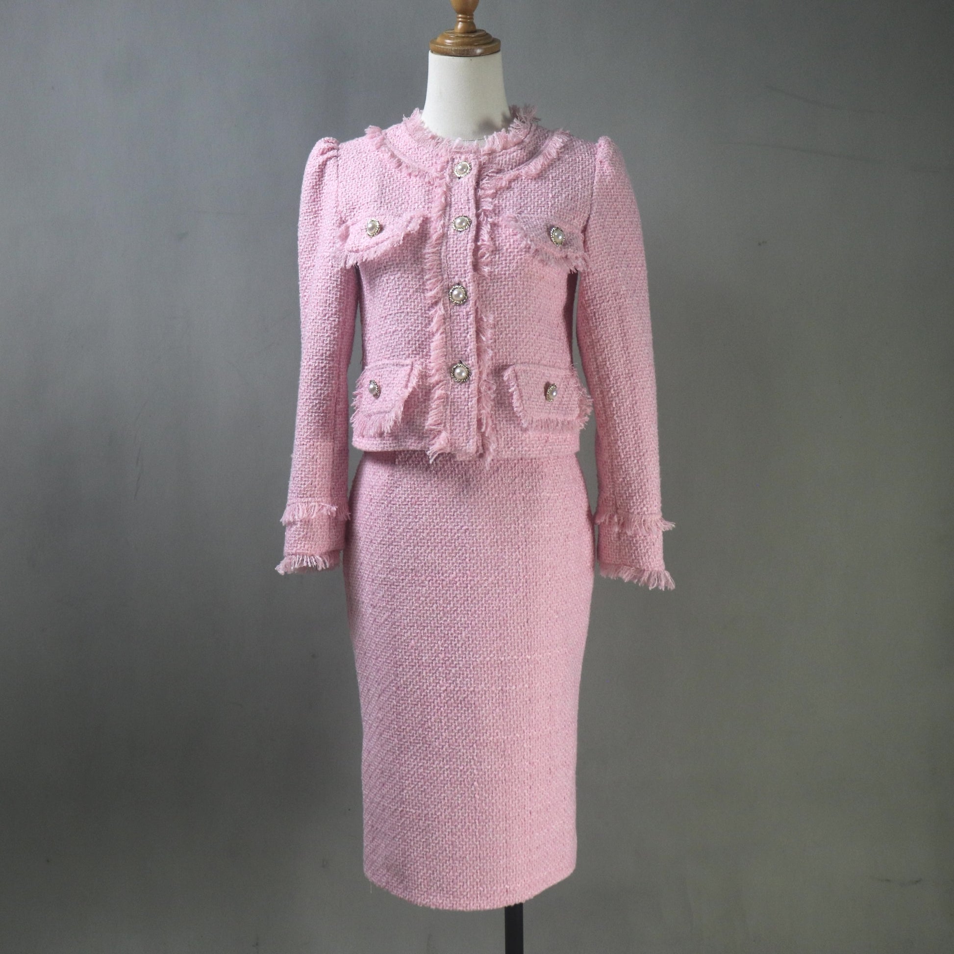 Pink tweed suit on a mannequin against a gray background