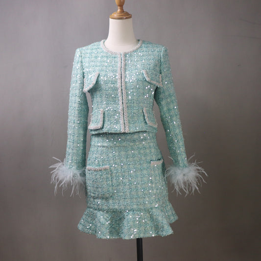 Custom aqua sequin tweed skirt suit for women featuring a fitted jacket with feather cuffs, matching ruffled skirt, and decorative trim displayed on mannequin.