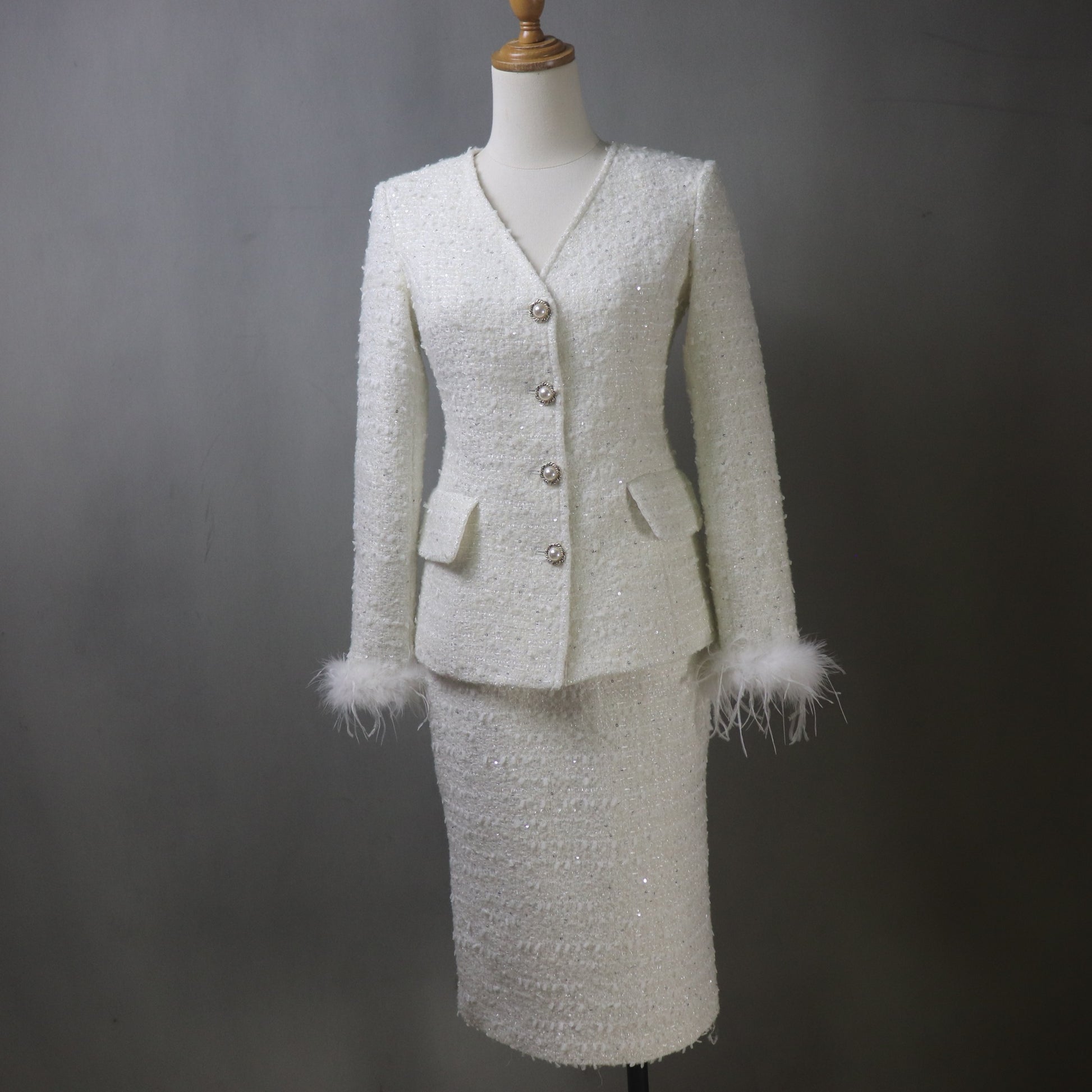 White tweed suit with feathered cuffs on a mannequin against a gray background